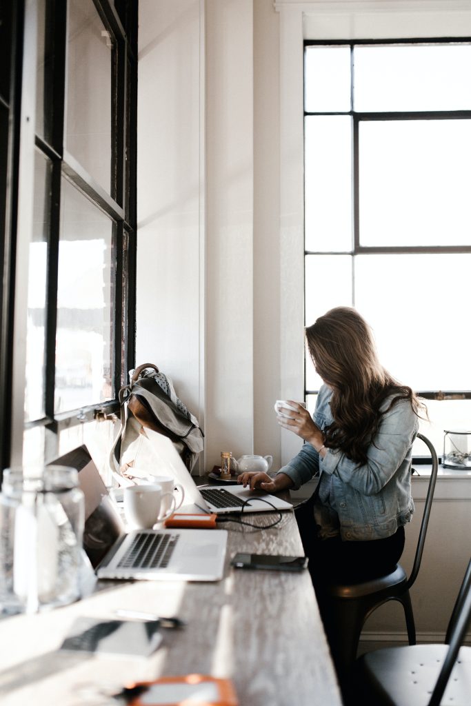 Una mujer trabaja en su computadora mientras toma un café.